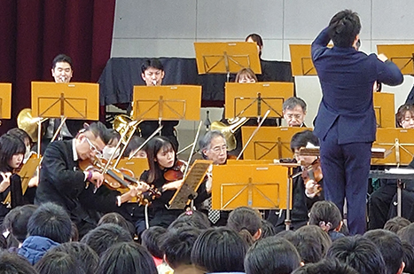 小学校体育館で、オーケストラ演奏を熱心に聴く児童